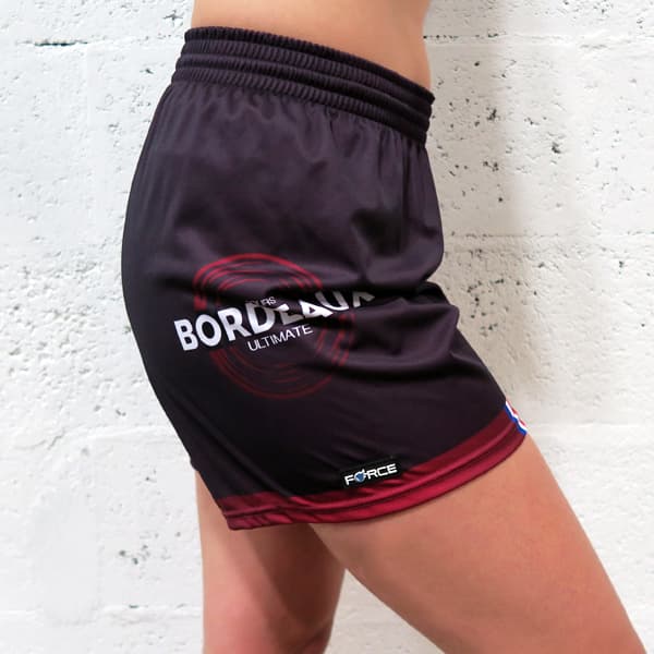 vue de profil droit du bas du corps d'une femme portant un short noir féminin devant un mur blanc