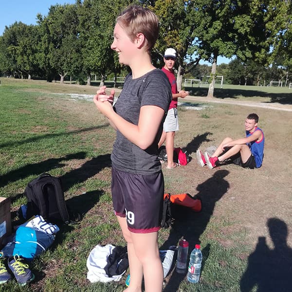 femme souriante sur un terrain de sport en herbe portant un tshirt et short noirs
